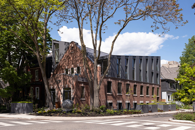 A brick building with a geometric black addition on the corner of a tree lined street