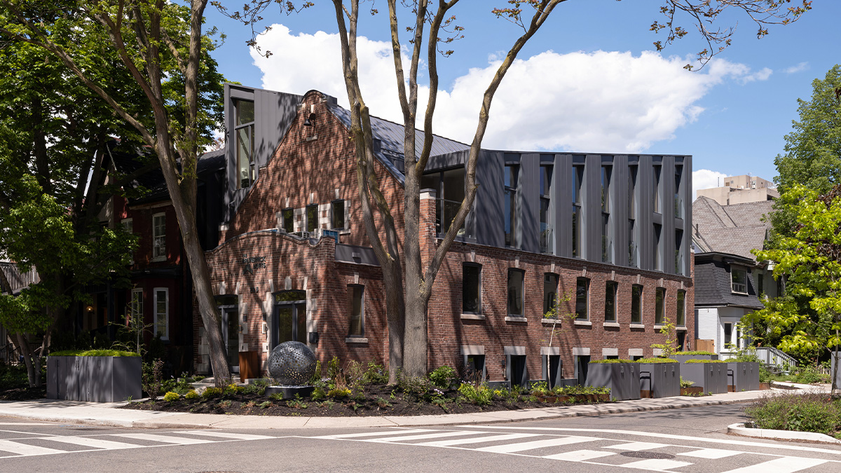 A brick building with a geometric black addition on the corner of a tree lined street