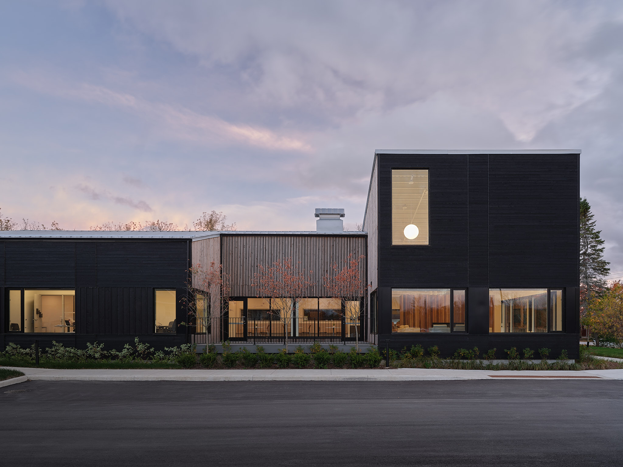A modern, low-rise building with dark exterior siding and large windows, shown at dusk
