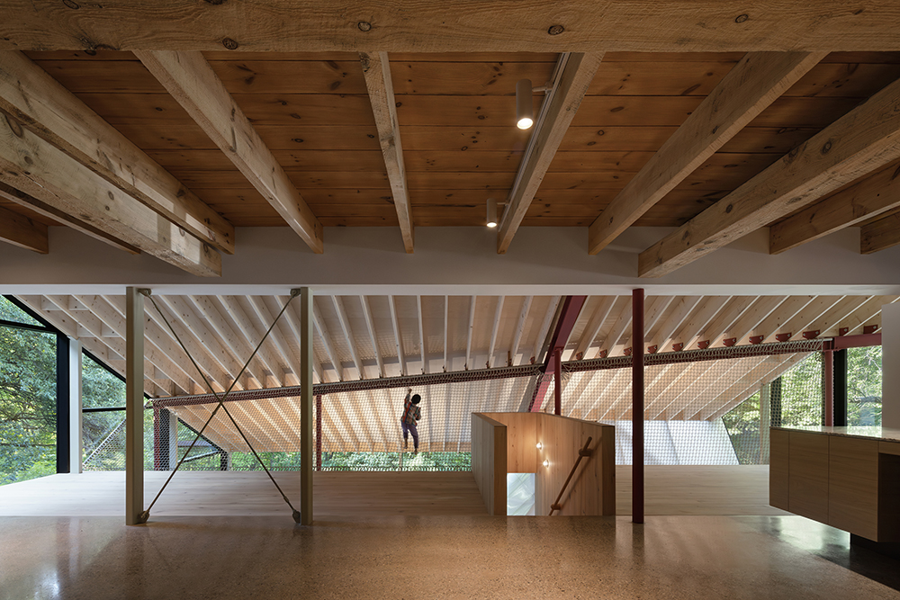 A large open space with polished floods and wooden roof rafters, there is a net suspended over an open atrium space and a child crawling on the net