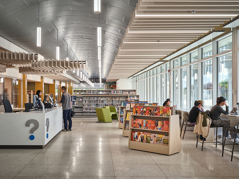 The interior of a library space with an undulating metal ceiling and low bookshelves