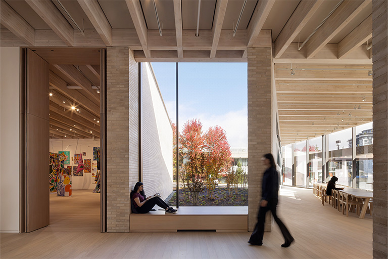 A large window in a sharply angled room with exposed roof structure and tan bricks