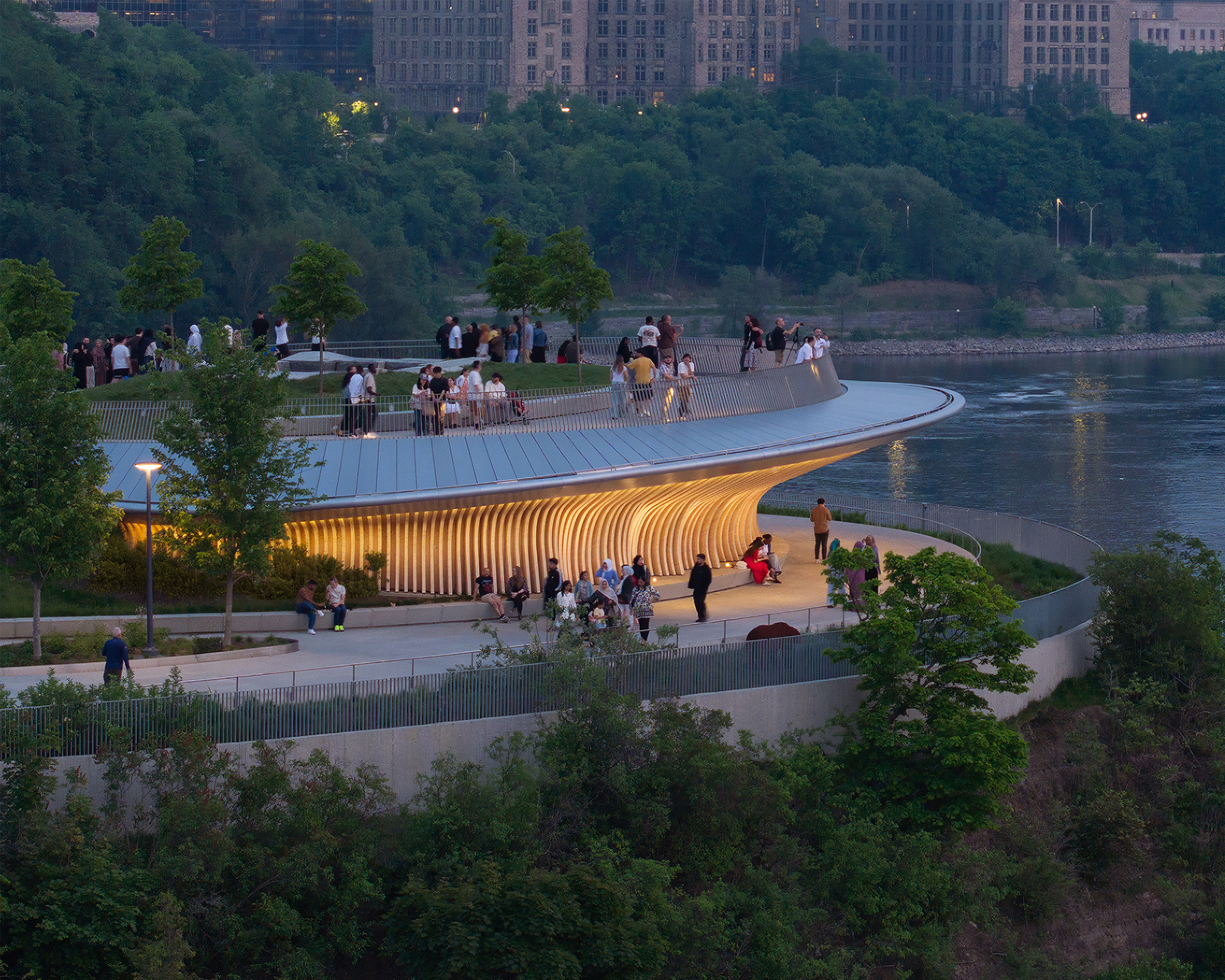 A curved, elevated waterfront overlook with a glowing underside, surrounded by trees and walking paths