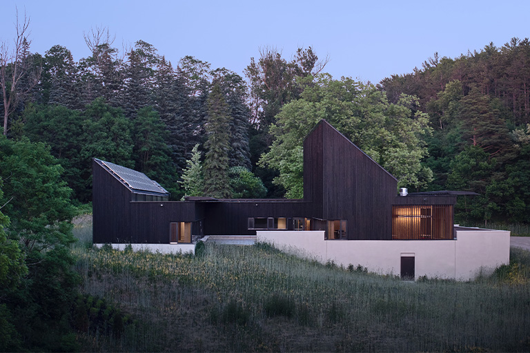 A geometric building with dark wood siding and angled rooflines, set on a grassy hillside