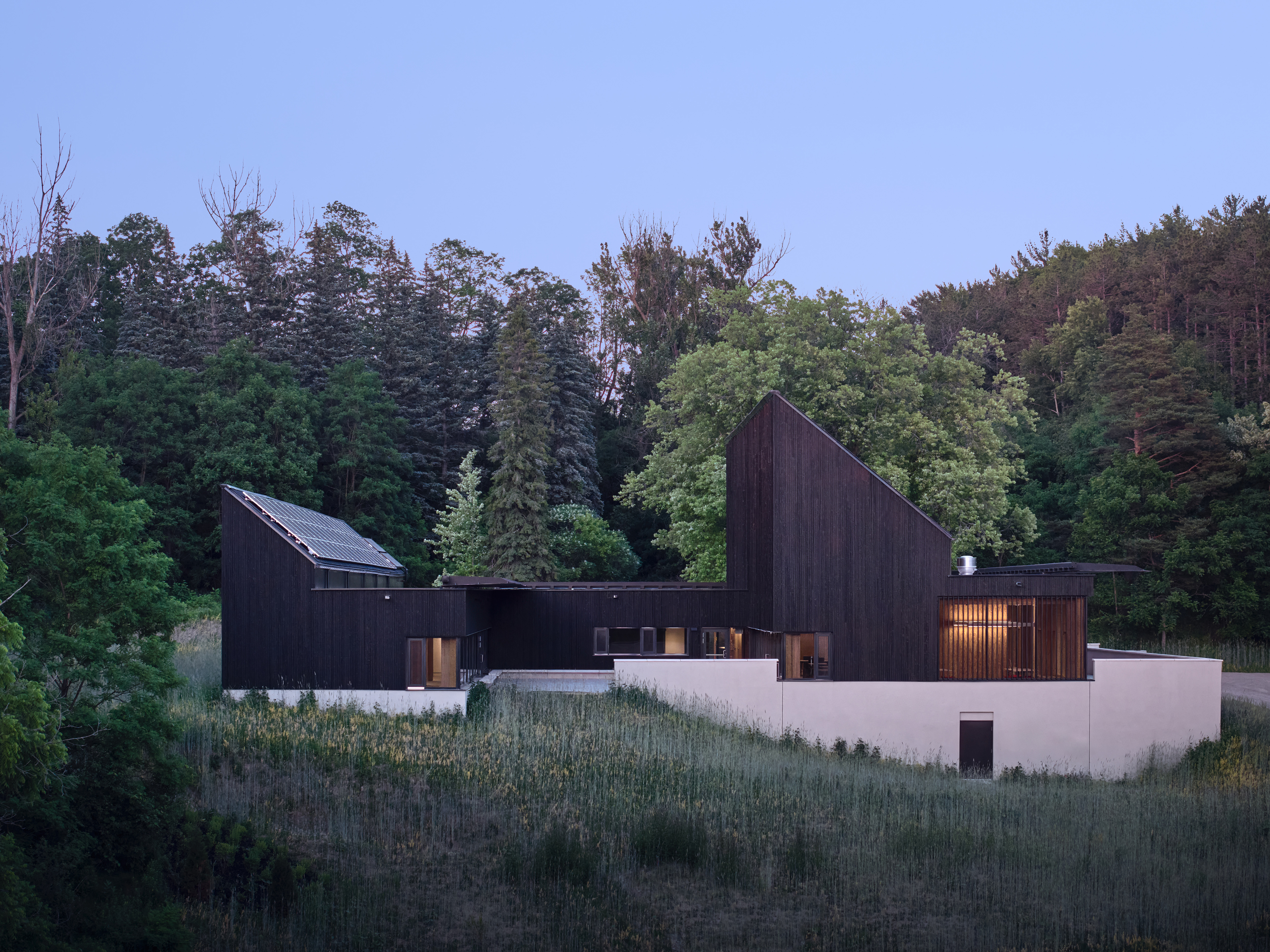 A geometric building with dark wood siding and angled rooflines, set on a grassy hillside