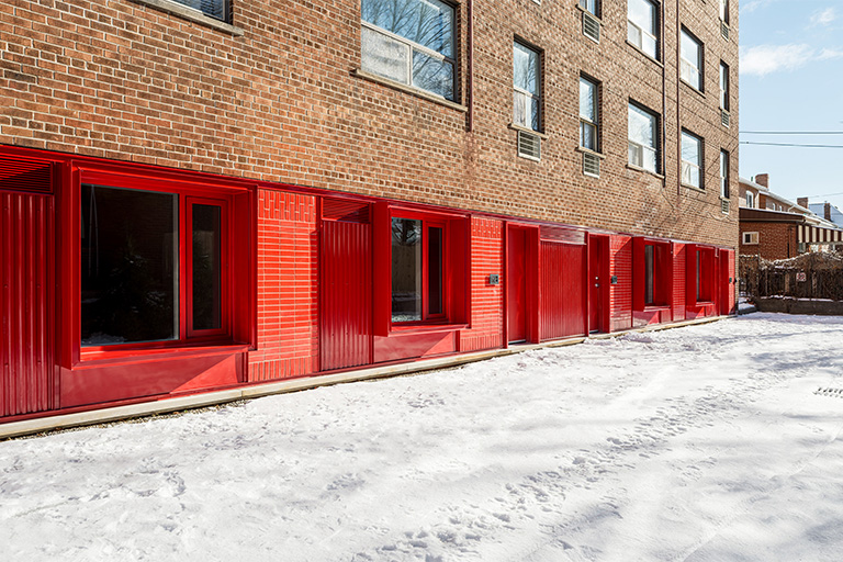 A brick apartment building with a row of bright red ground‑floor window frames and doors