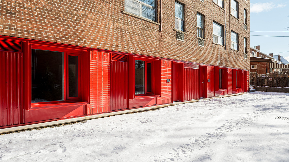 A brick apartment building with a row of bright red ground‑floor window frames and doors