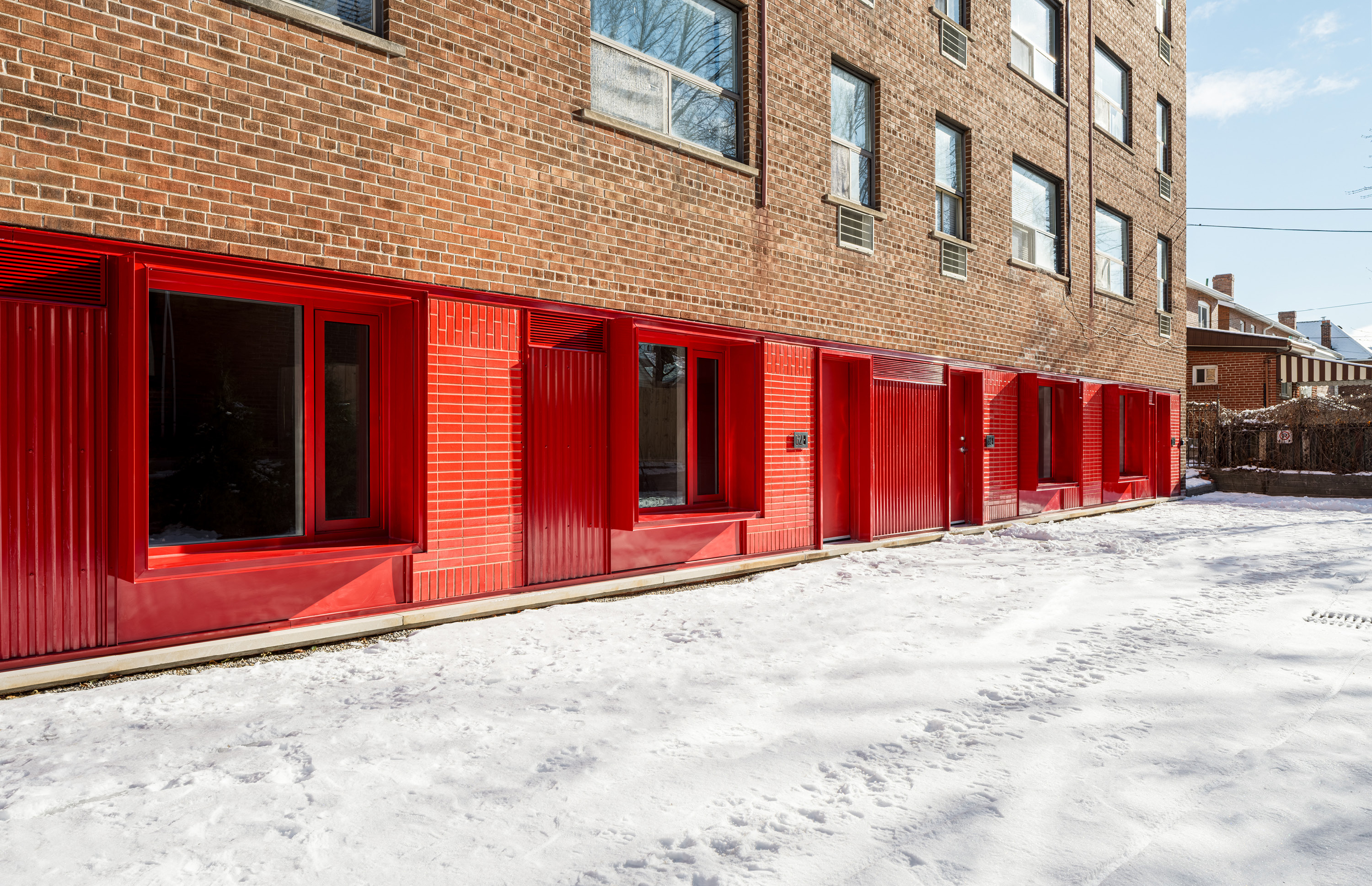 A brick apartment building with a row of bright red ground‑floor window frames and doors