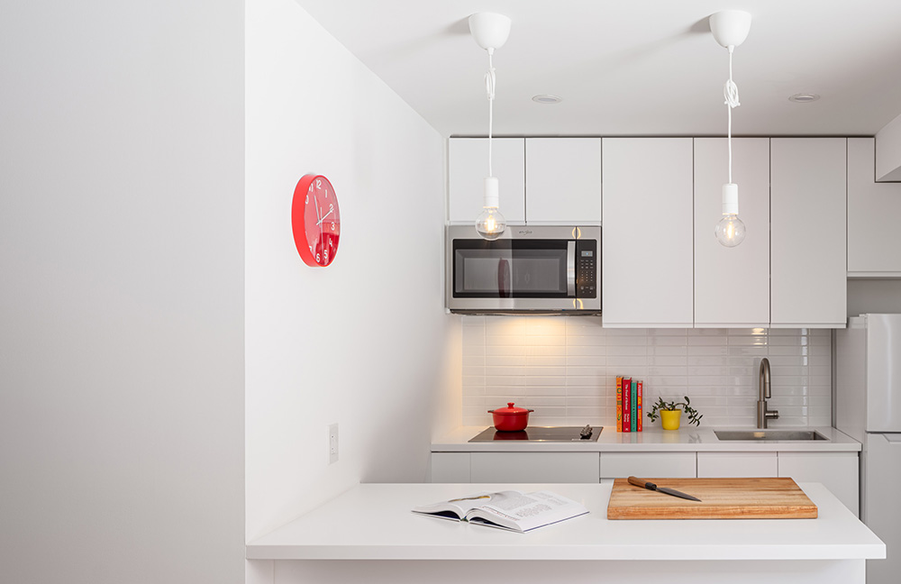 A simple white kitchen with sleek finishes and a red clock on the left wall