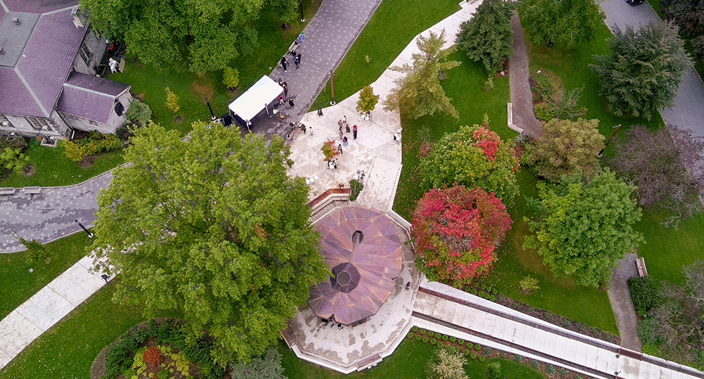 An aerial view of a park with autumn trees, walkways, and a circular pavilion at the center