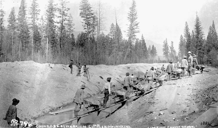 Carrying wheelbarrows filled with stone, a row of workers cross a narrow beam spanning a ditch.