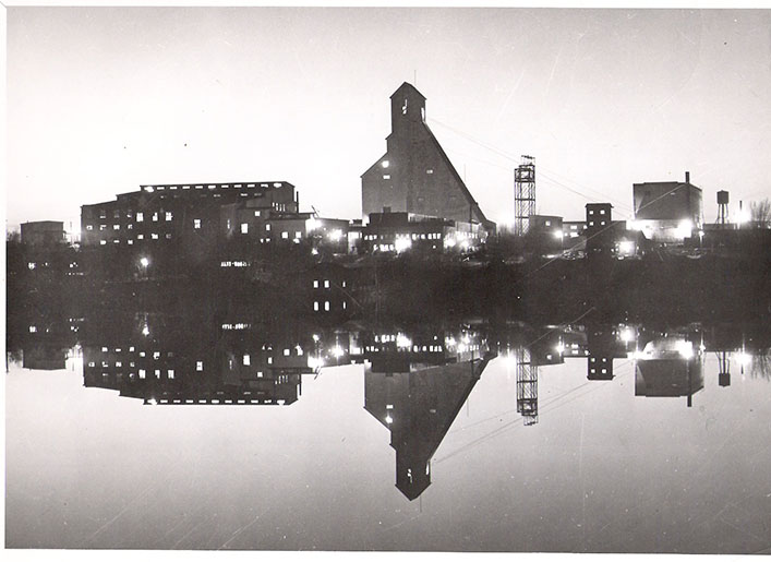 Various mining structures including large headframe reflected onto the surface of a lake
