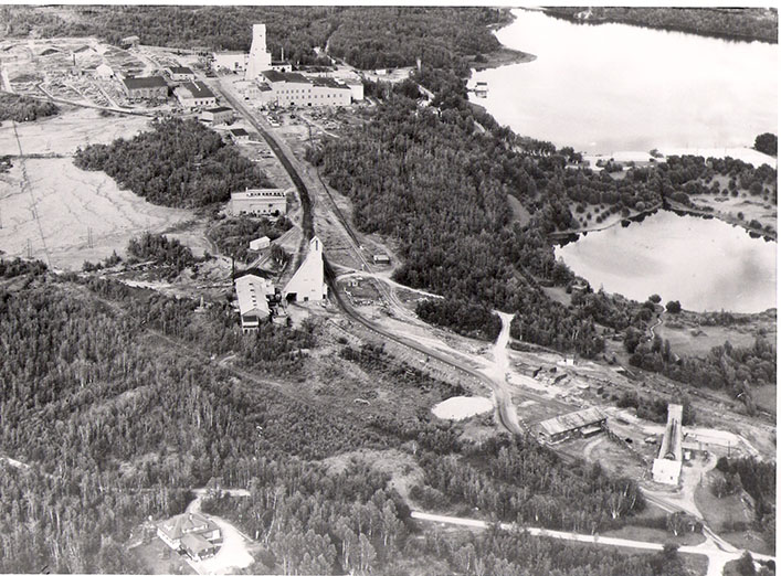 Mining site in forested landscape, with three headframes and a road between them
