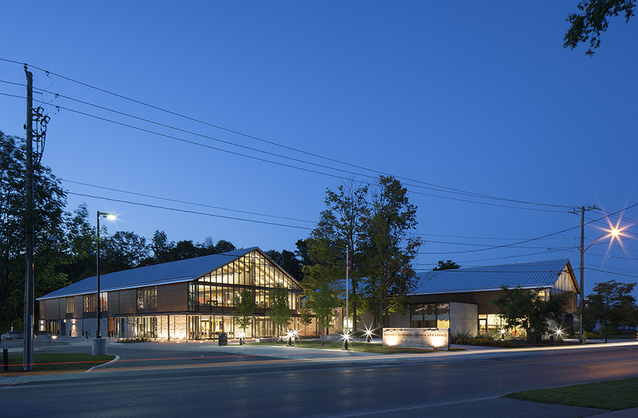 Large, curved, metal-clad structure with curtain wall windows adjoining a rectangular metal and glass building.