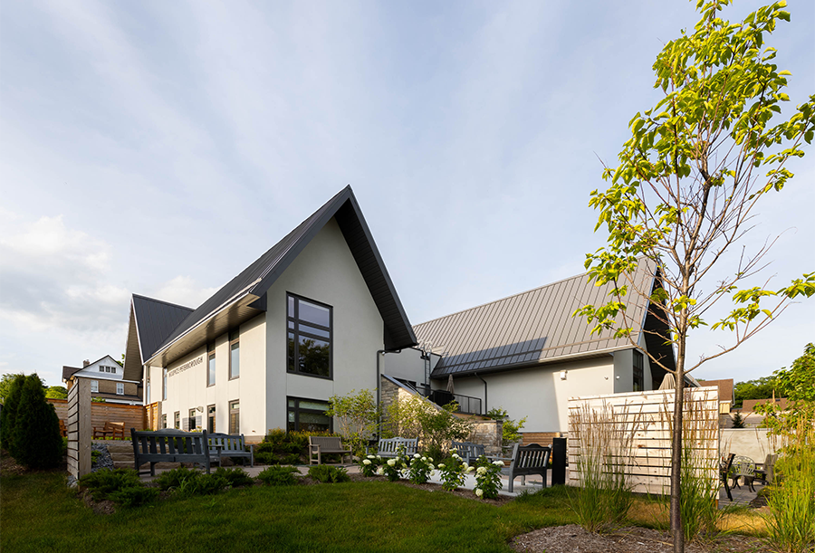 A two-storey log-clad house with gabled roofs set within a woodsy landscape of mature trees.