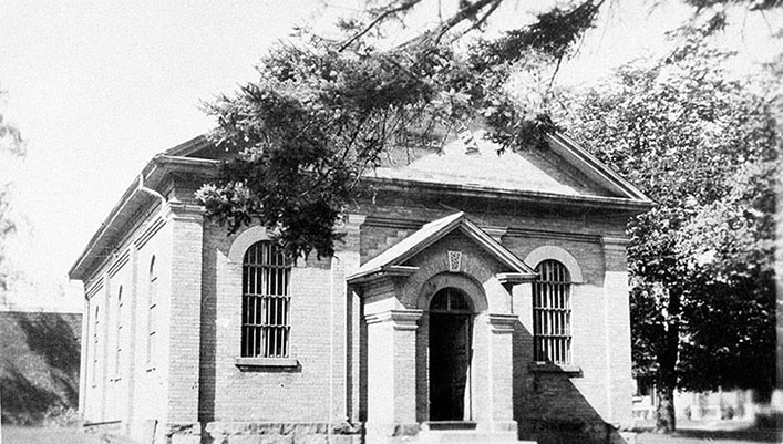 Black and white photograph showing the former land registry office in Whitby, with neoclassical features such as round-arched windows and a projecting portico. A tree branch is in the foreground. 