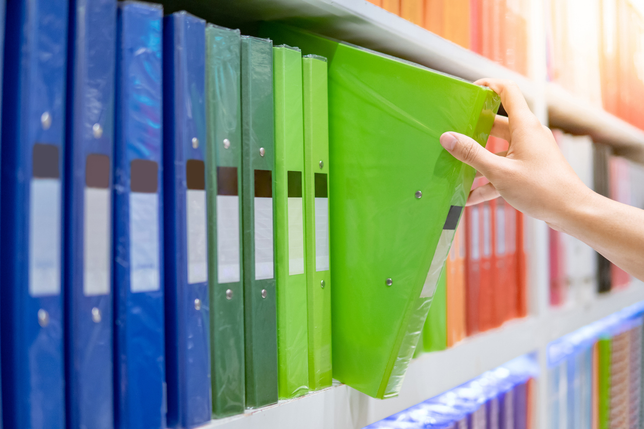 An individual taking a green binder from a white wall bookcase