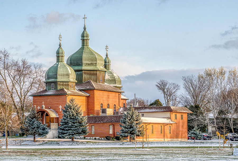 Perspective of a brick church with hip roofs and three onion domes projecting out of the top.