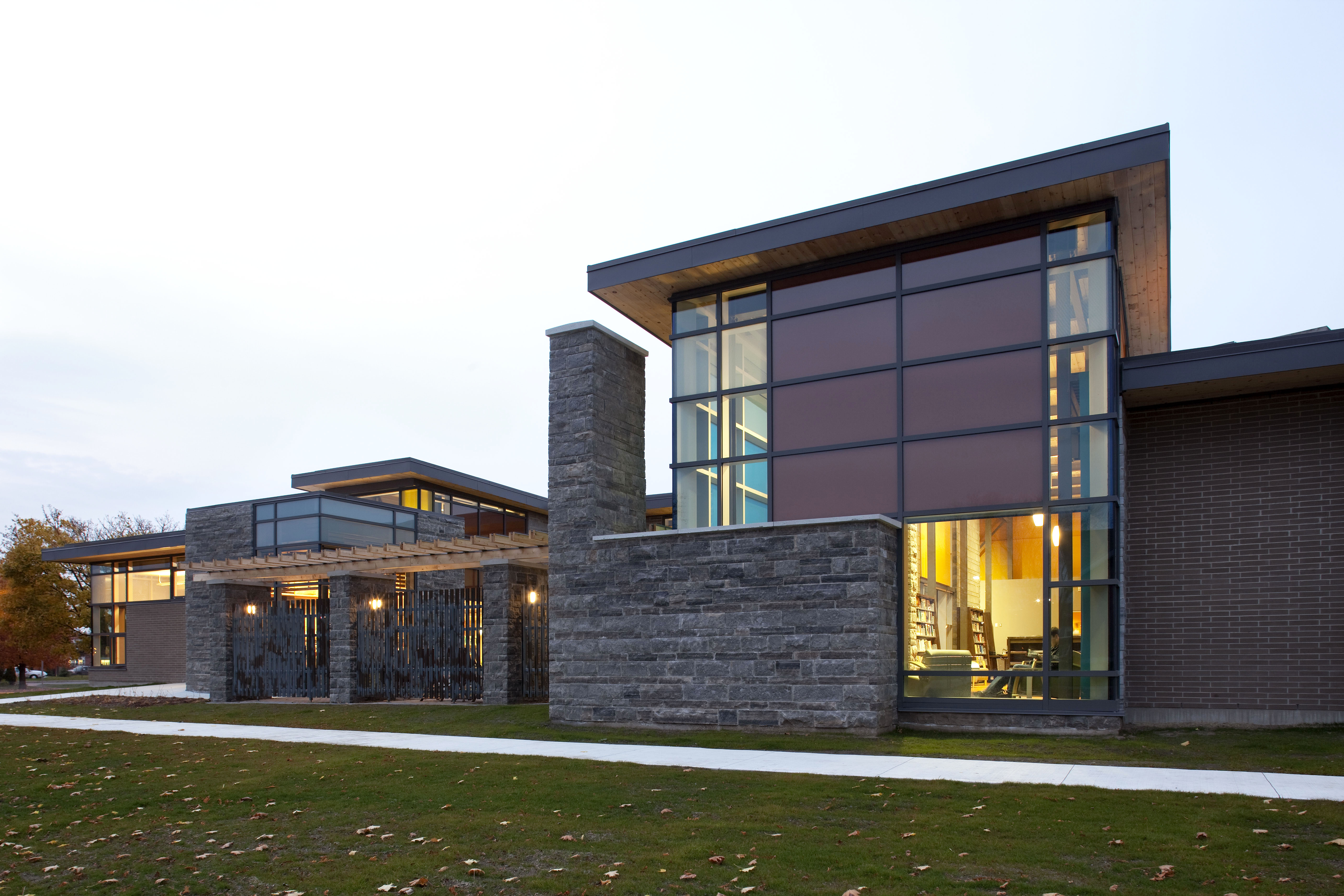 Evening view of the library showcasing a blend of glass, brick, and limestone, with warm interior lighting and a landscape in the foreground.